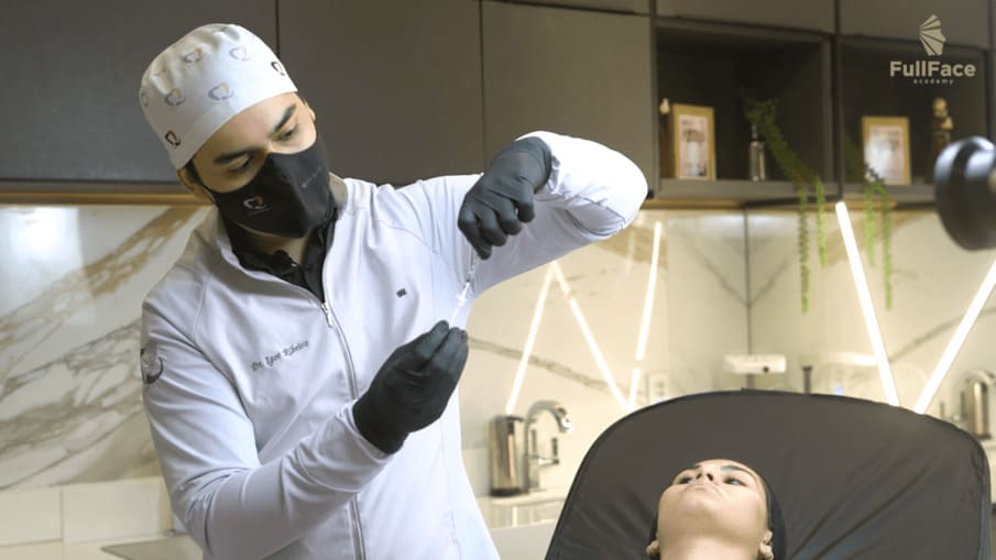 Médico de jaleco branco e máscara segura uma seringa sobre um paciente em um ambiente médico.