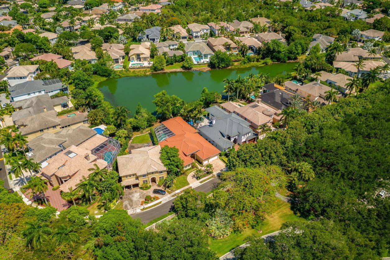 Aerial view of a suburban neighborhood with houses around a green pond and trees