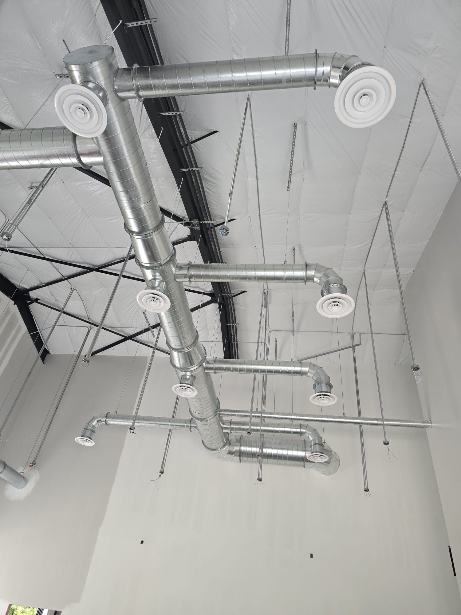 Ceiling view of exposed silver ductwork and round vents in an industrial interior