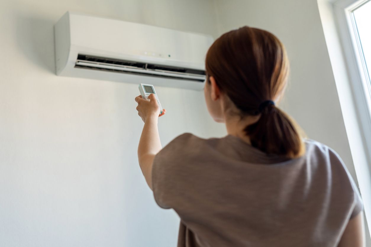 Person pointing a remote at a wall-mounted air conditioner in a bright room