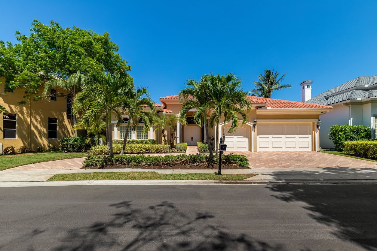 Suburban house with palm trees, a two-car garage, and a sunny street in front