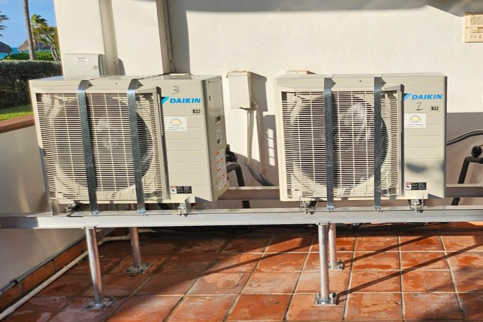 Two outdoor HVAC units on a metal platform beside a white wall