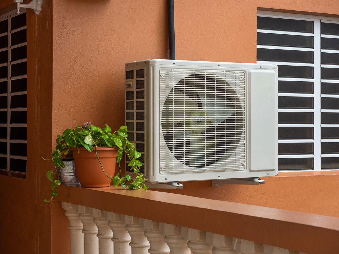 Wall-mounted air conditioner on an orange balcony beside a potted plant and window