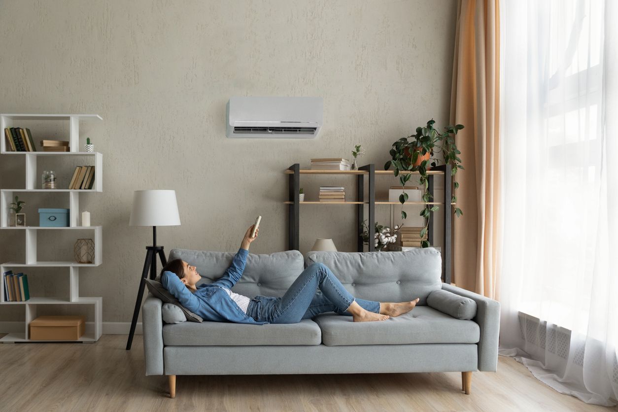 Person pointing a remote at a wall-mounted air conditioner in a bright room