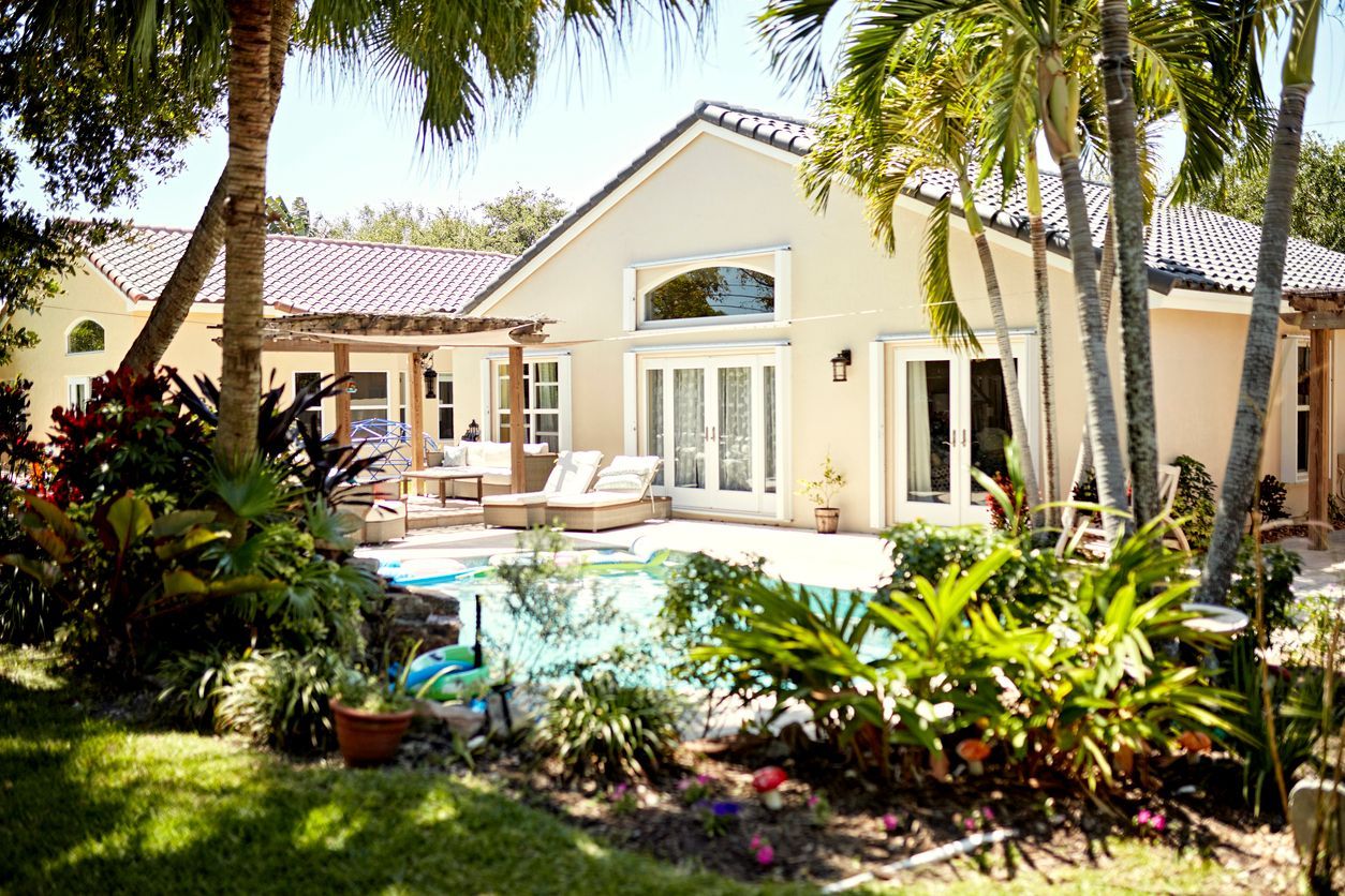 Tropical villa with a pool, palm trees, and a patio with lounge chairs and bright greenery