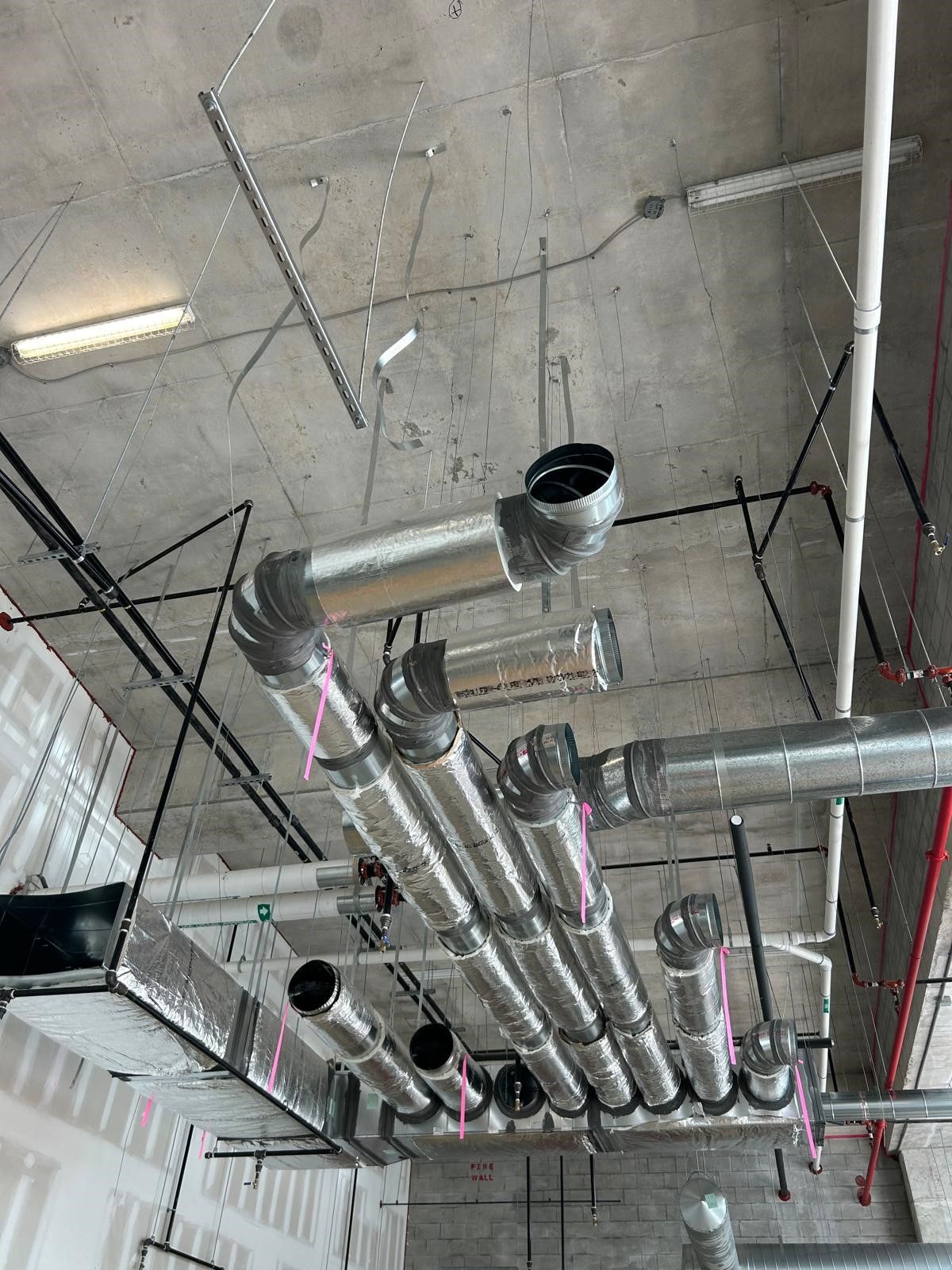 Ceiling with exposed silver HVAC ducts and pipes in an industrial interior