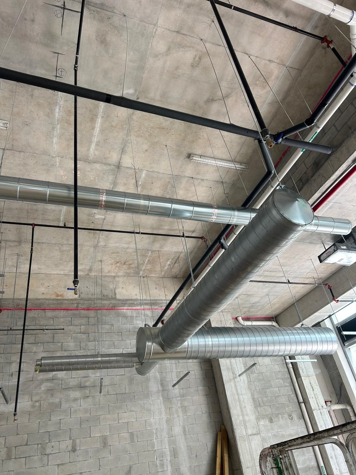 Ceiling with exposed industrial pipes, ducts, and metal framing in a concrete building interior