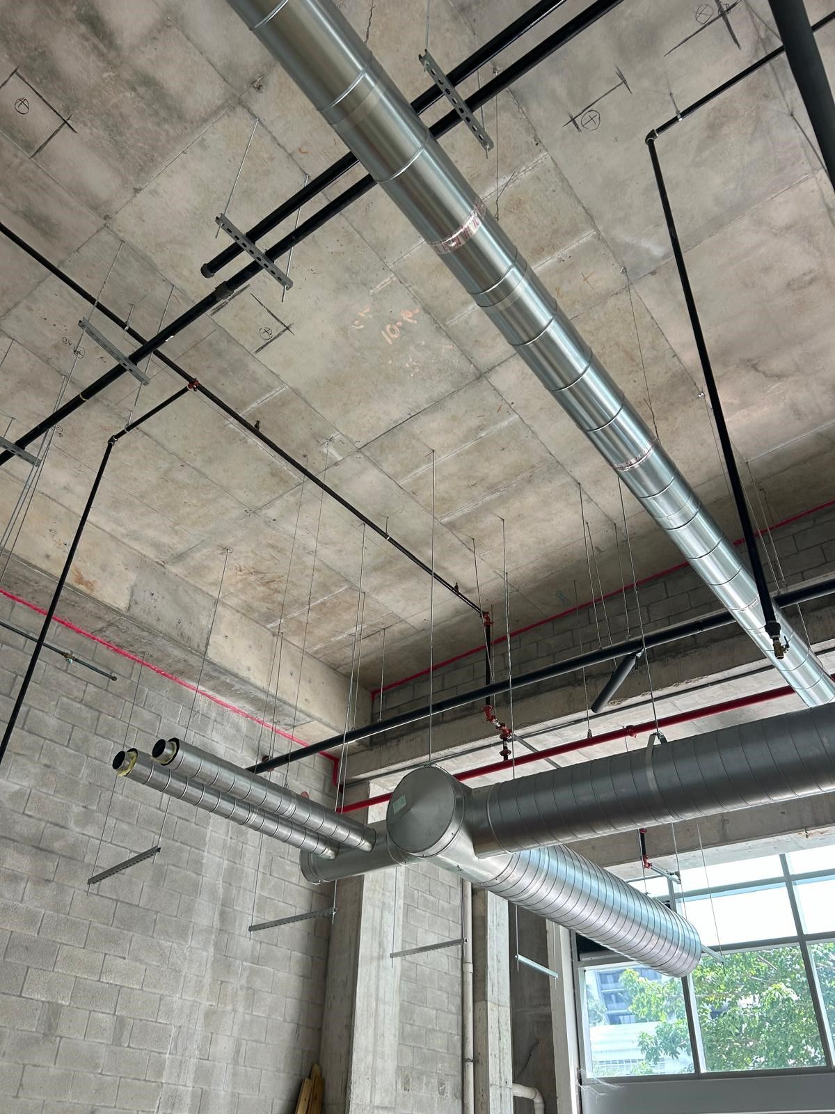 Exposed concrete ceiling with HVAC ductwork and piping above a large window in an unfinished room