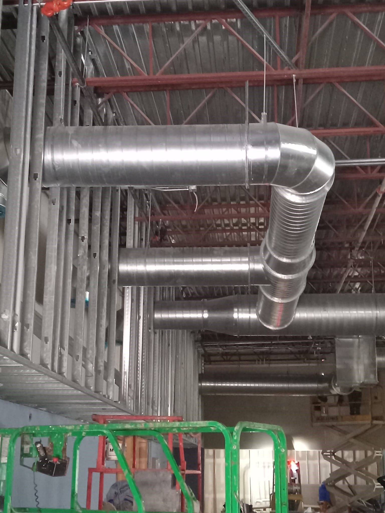 Silver ventilation ducts in an industrial ceiling above green machinery.
