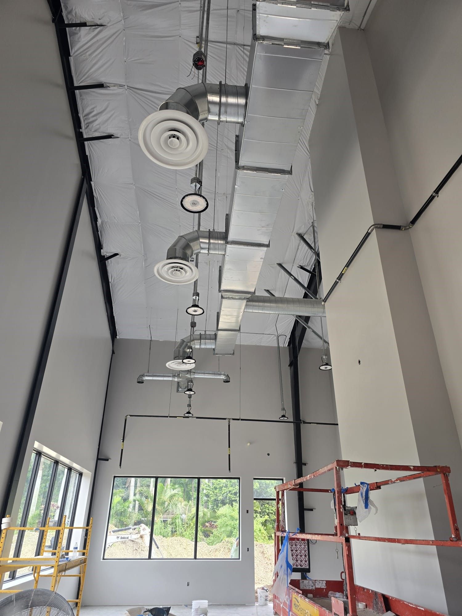 Industrial interior with exposed ceiling ducts, windows, and a red scaffolding frame.