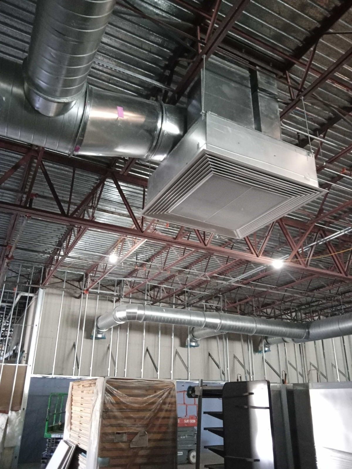 Industrial warehouse ceiling with exposed ductwork, metal beams, and a large suspended HVAC unit