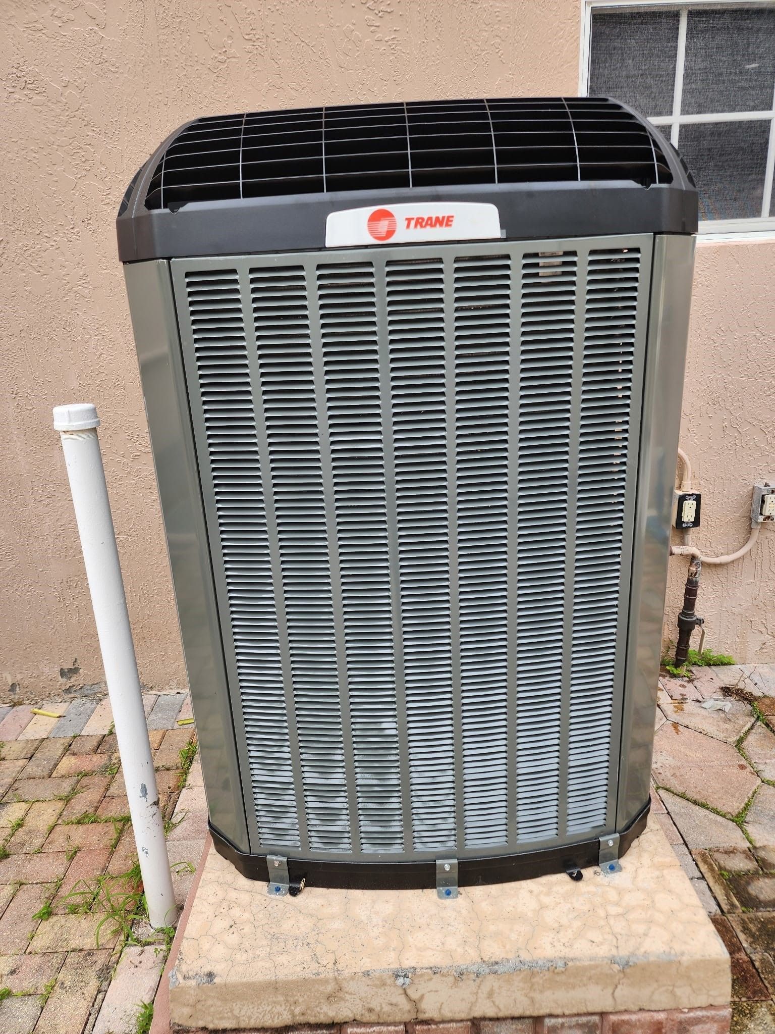Front view of a Trane outdoor air conditioner unit on a concrete pad beside a wall