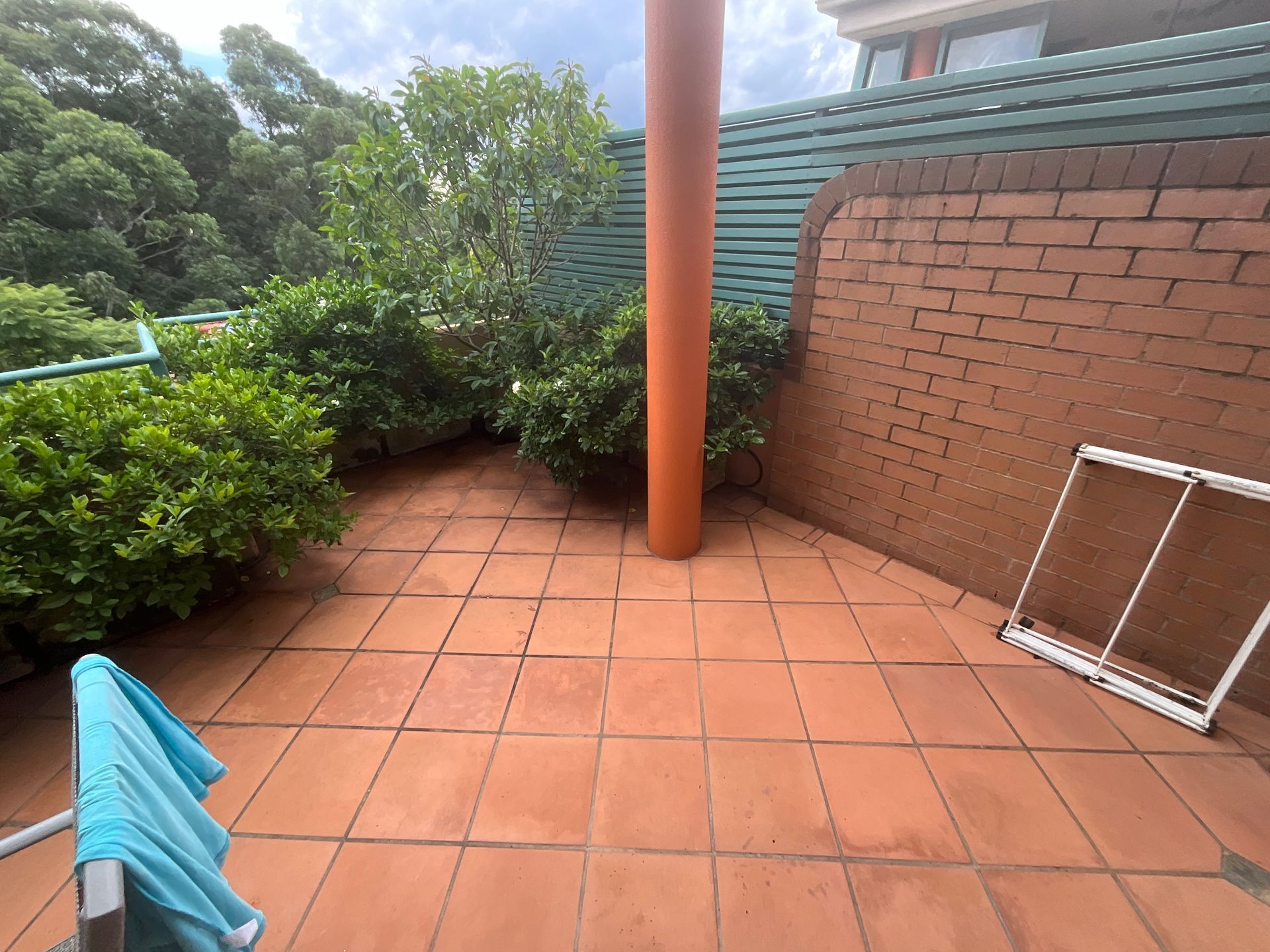 Terracotta patio with orange column, brick wall, green shrubs, and a small tilted white frame.