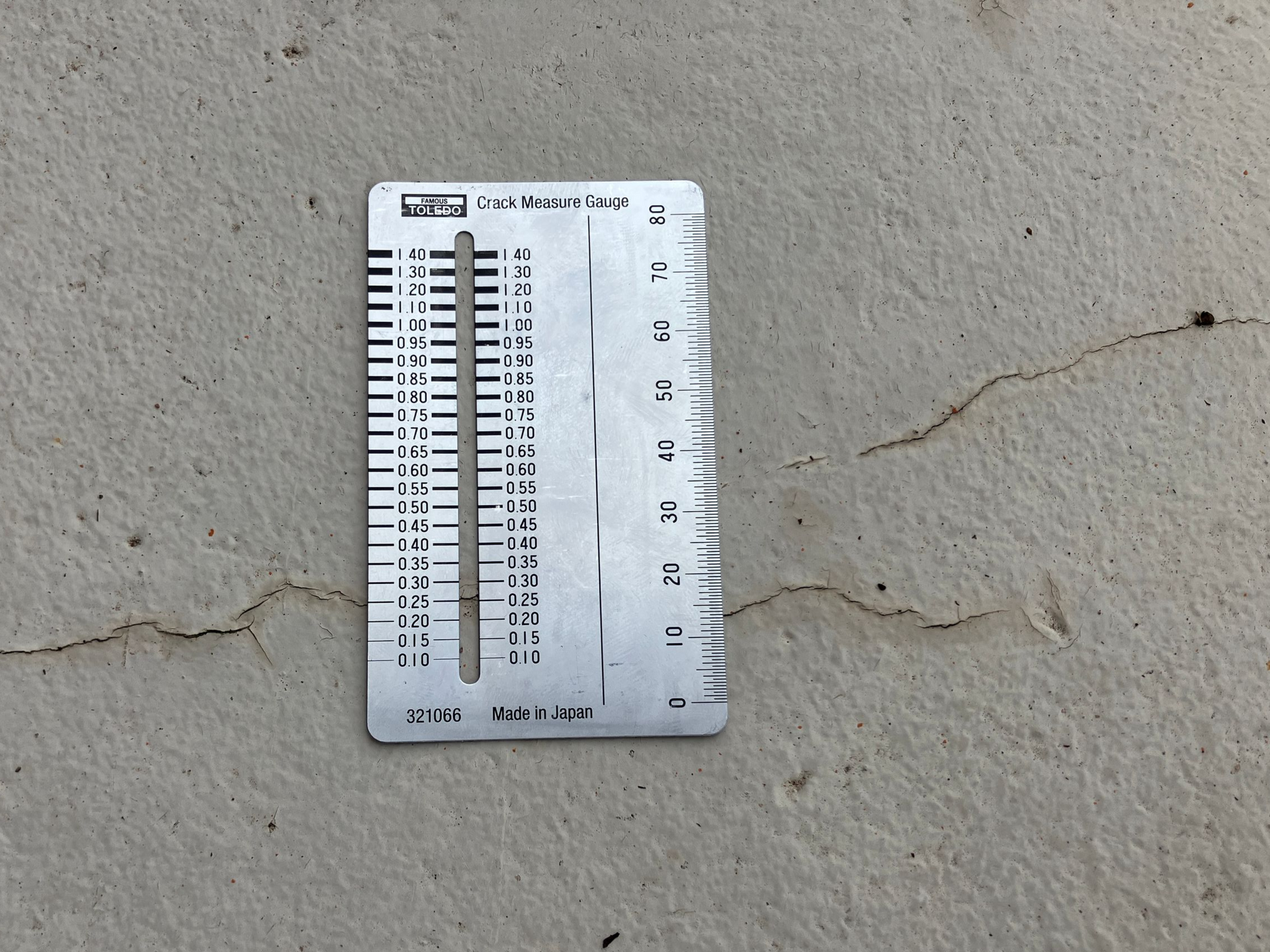 Small white ruler and soil moisture meter on concrete with a visible crack.