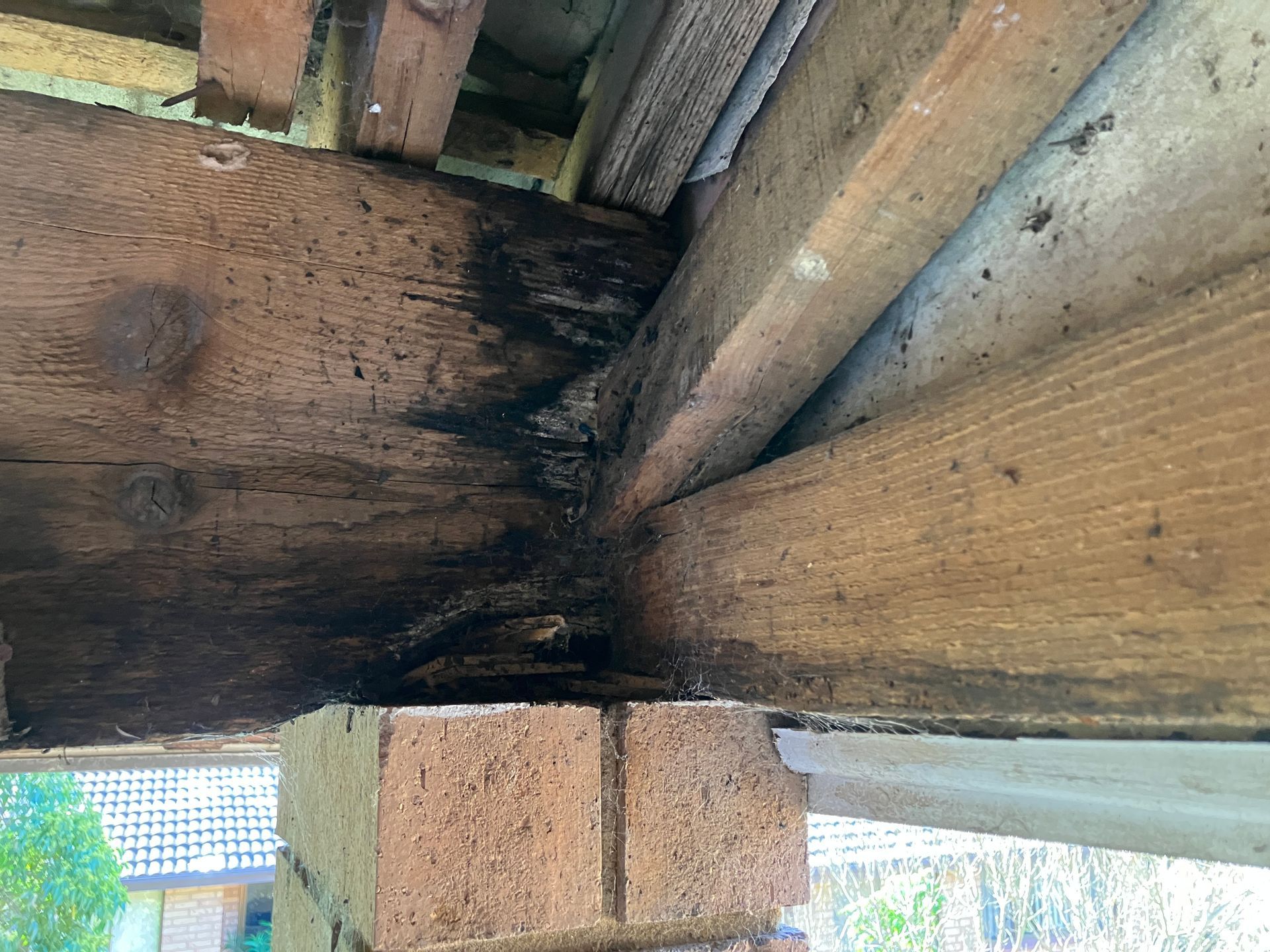 Close-up of a wooden roof beam joint with dark water damage and a brick support below