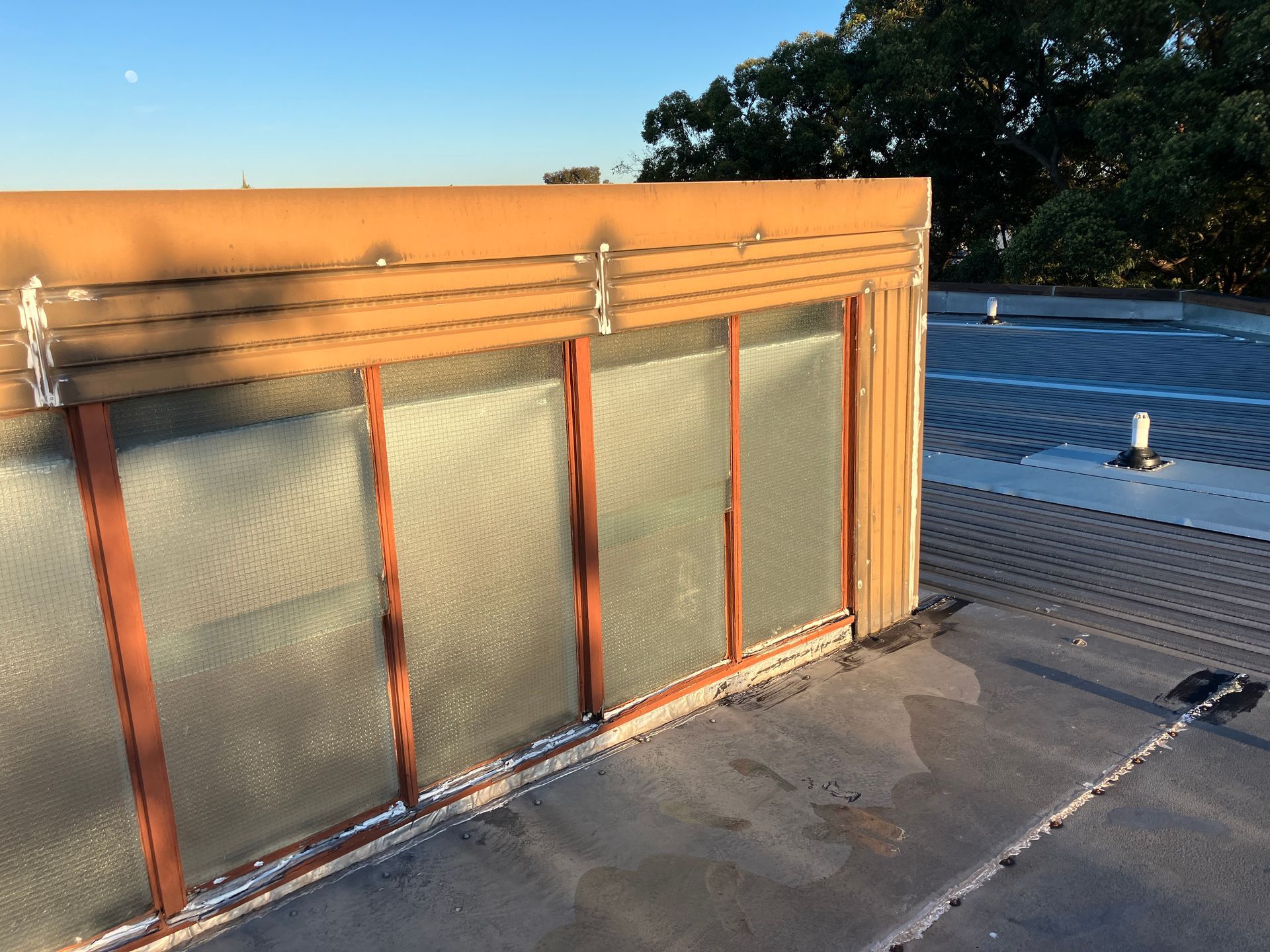 Rooftop HVAC enclosure with frosted panels and orange trim beside a flat roof under clear sky.