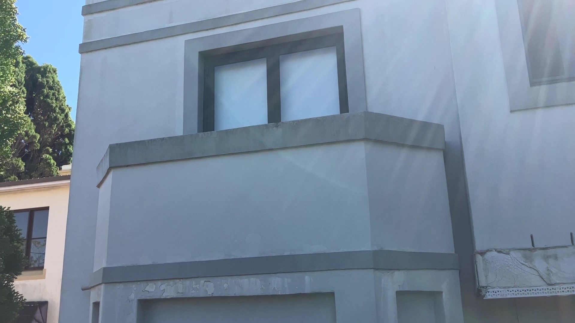 Gray two-story house facade with a small balcony and windows in bright sunlight