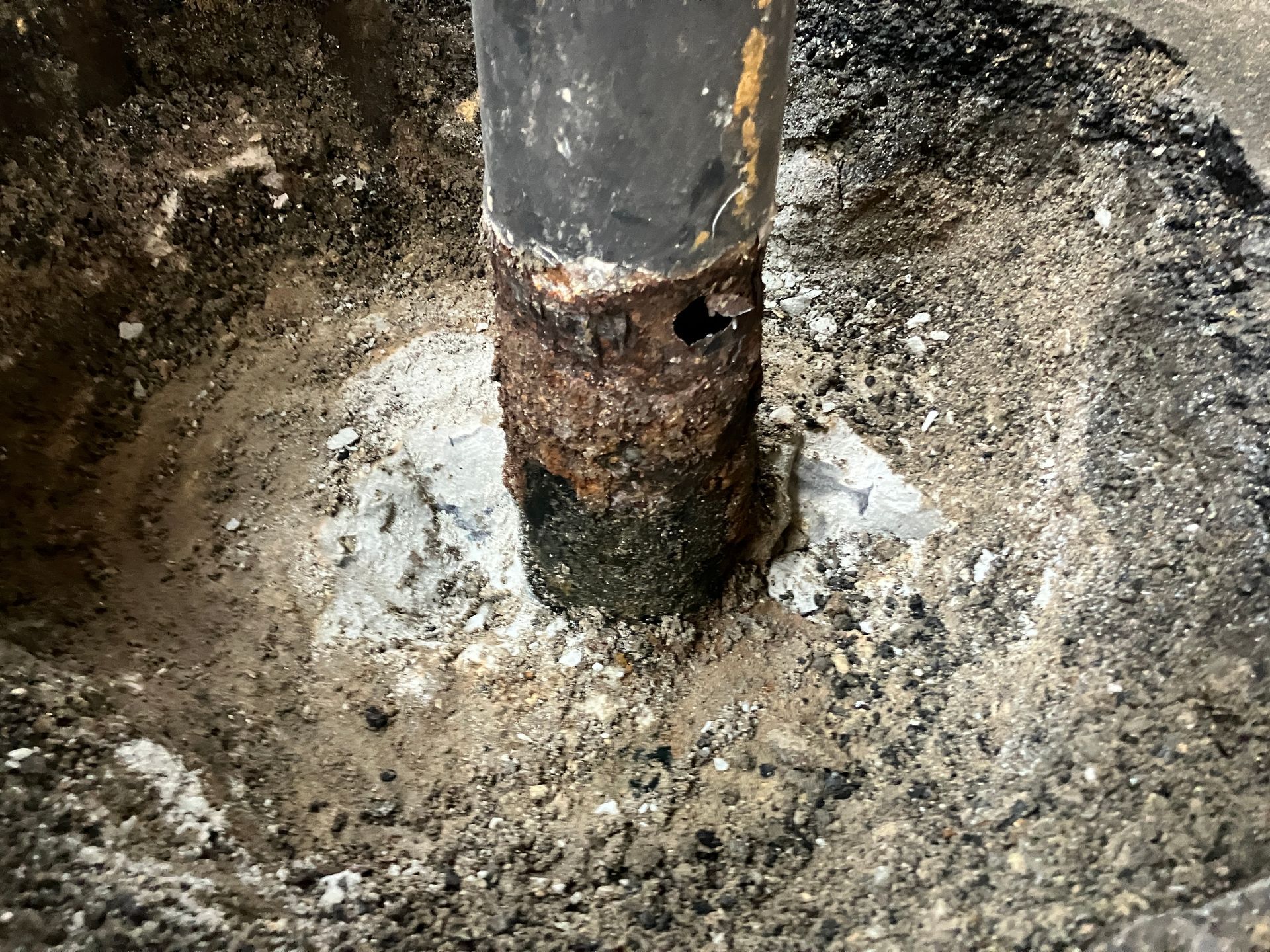 Rusty metal pipe in concrete with muddy water pooling around its base.