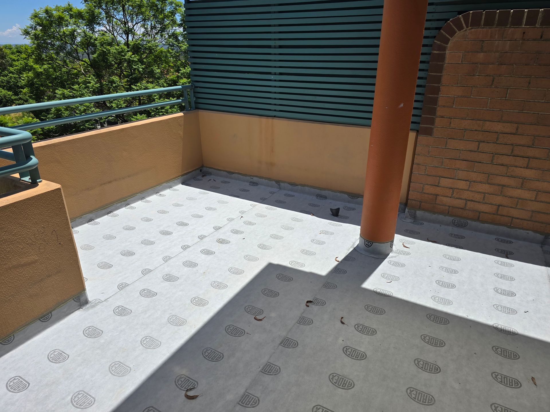 Sunlit rooftop terrace with patterned flooring, brick wall, and orange support pole