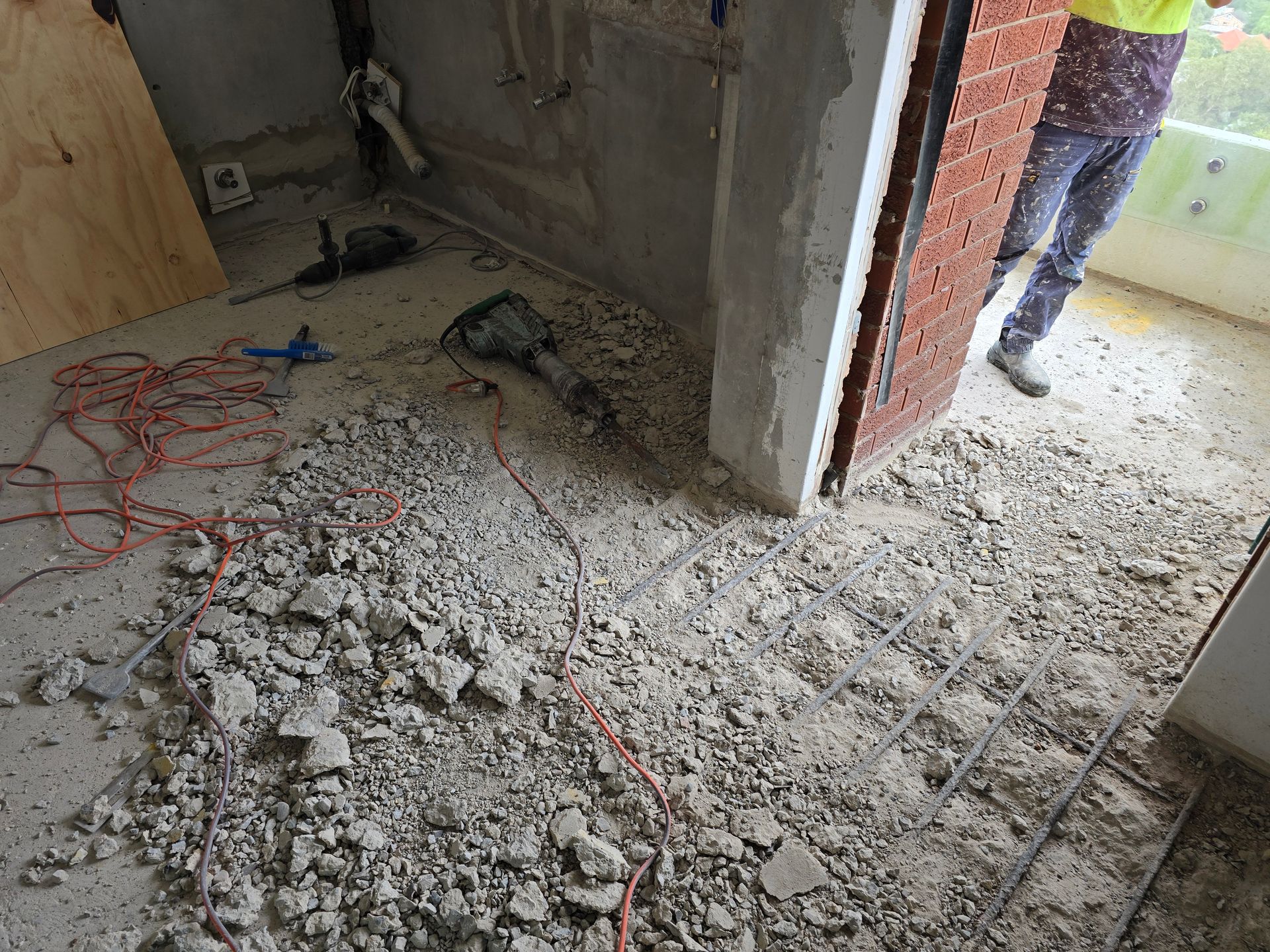 Construction site with rubble on the floor, exposed brick walls, and worker legs visible at the doorway.
