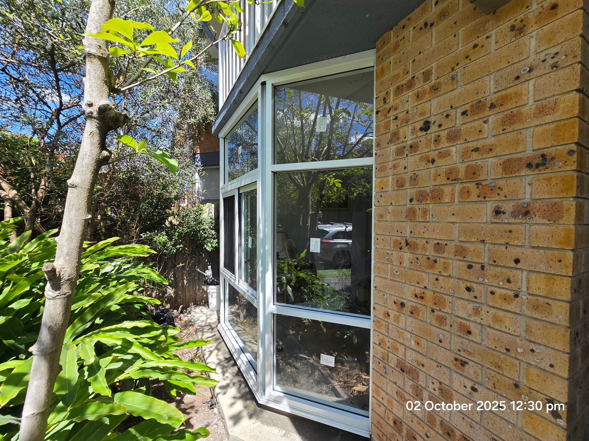 Side view of a brick house with large white-framed windows beside a leafy garden path
