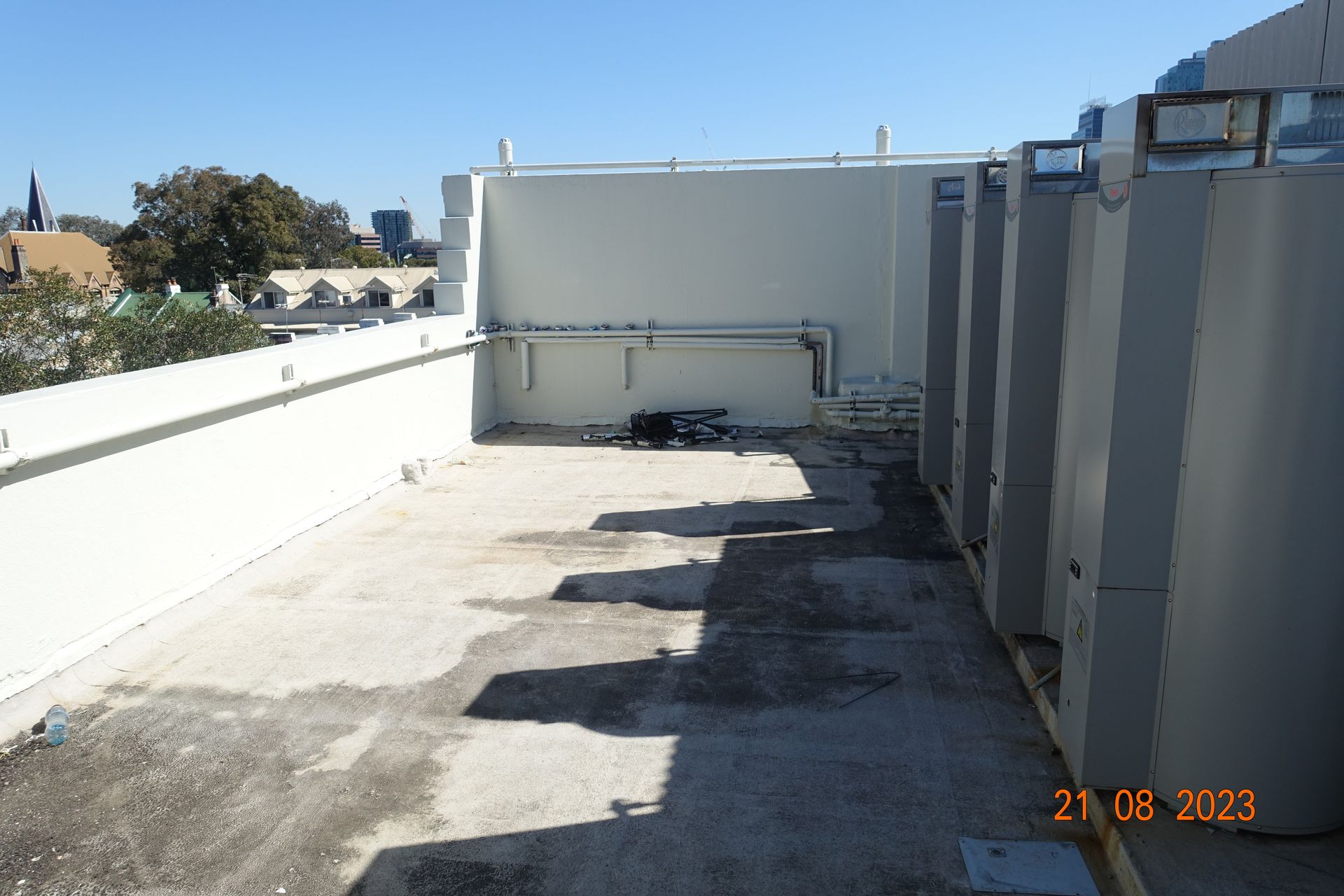 Rooftop with concrete surface, white parapet walls, and large gray HVAC units under a clear blue sky.