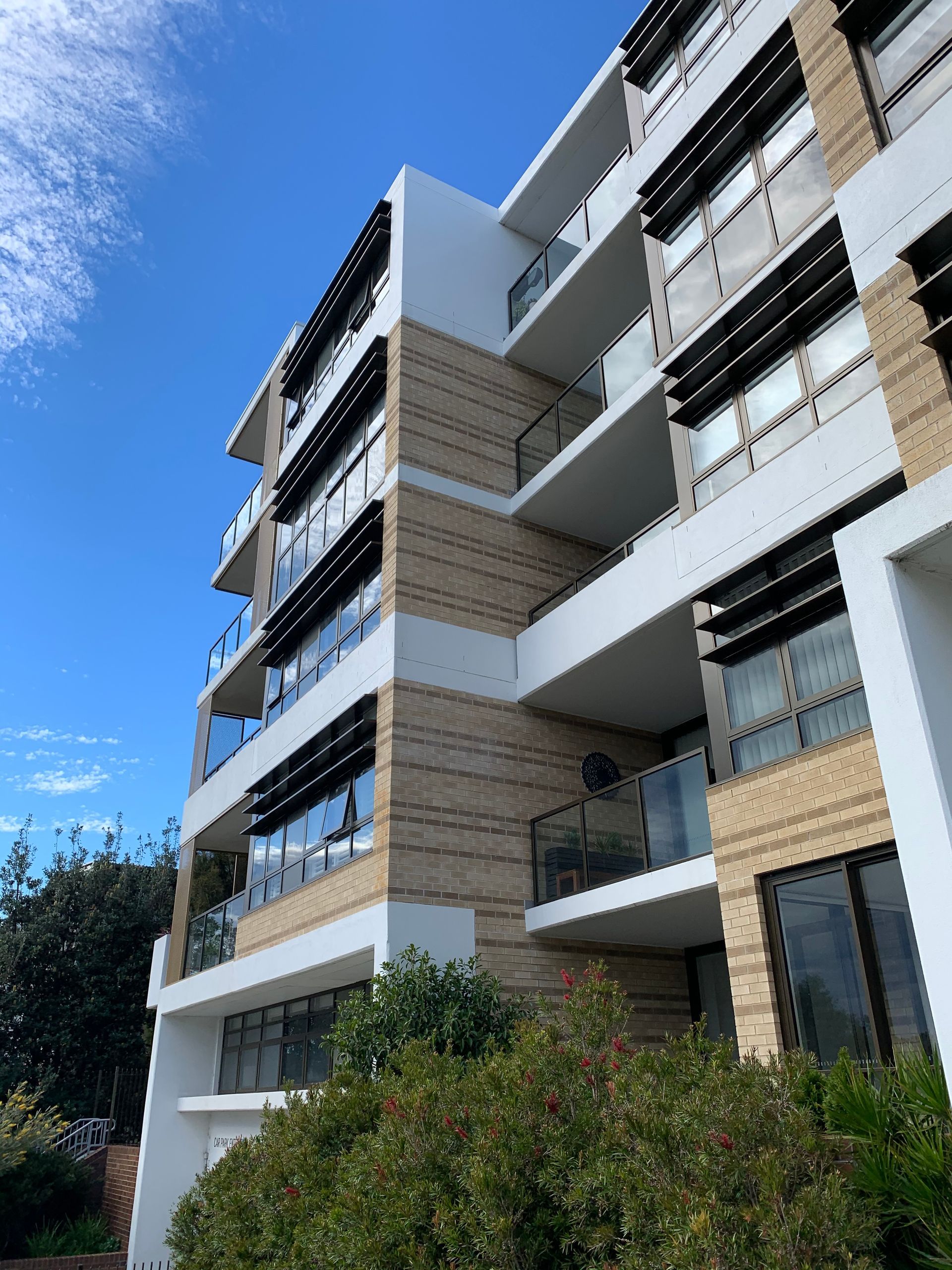 Modern apartment building with balconies and tan siding under a clear blue sky