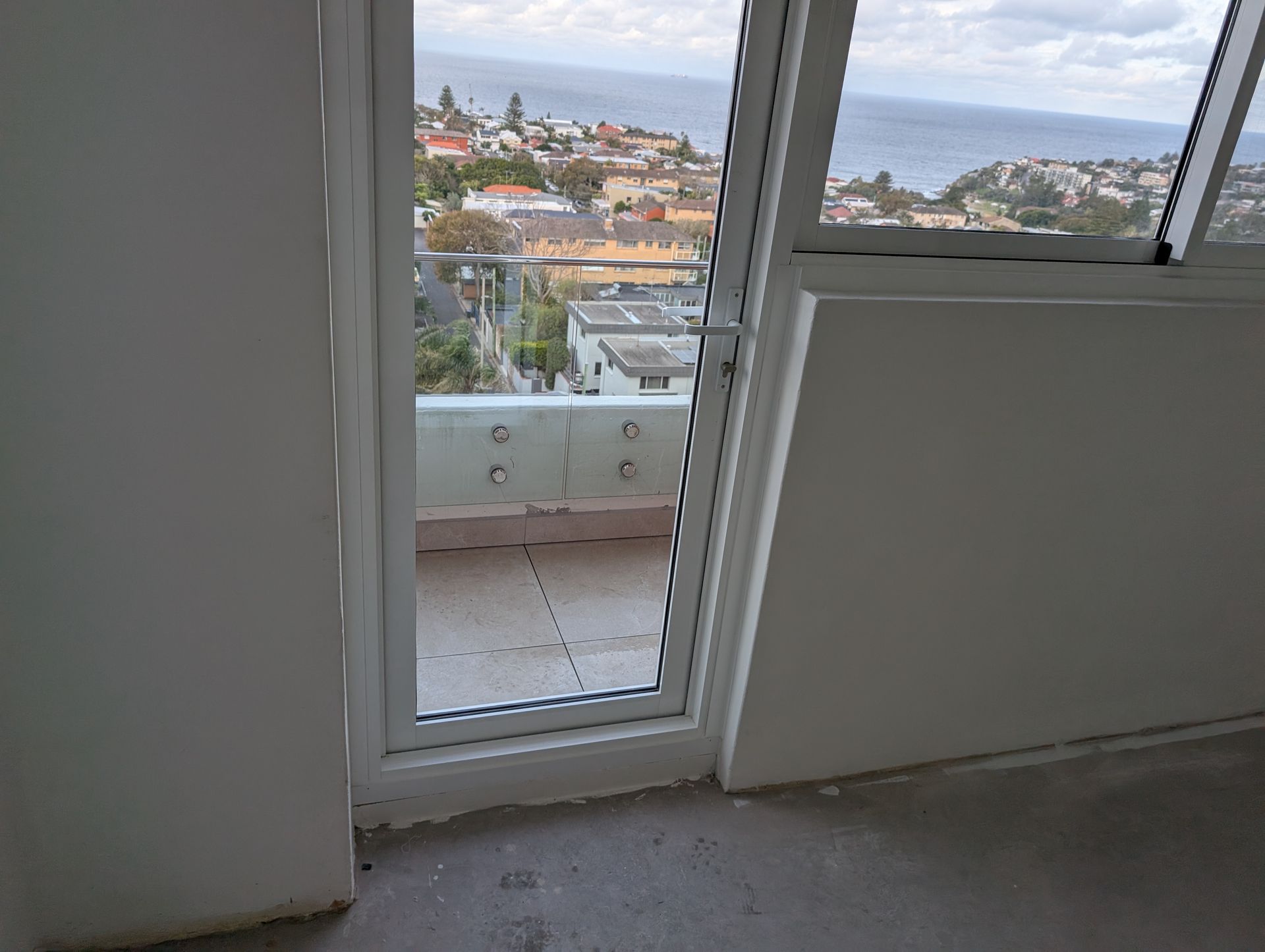 Open glass door to a balcony with a city and ocean view