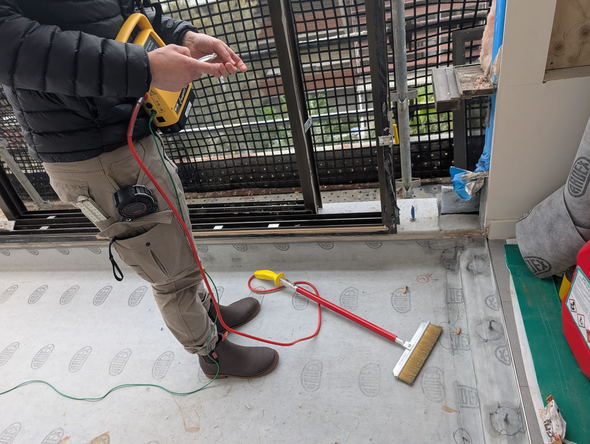 Worker using a cable tool on a concrete floor near a metal gate and broom indoors