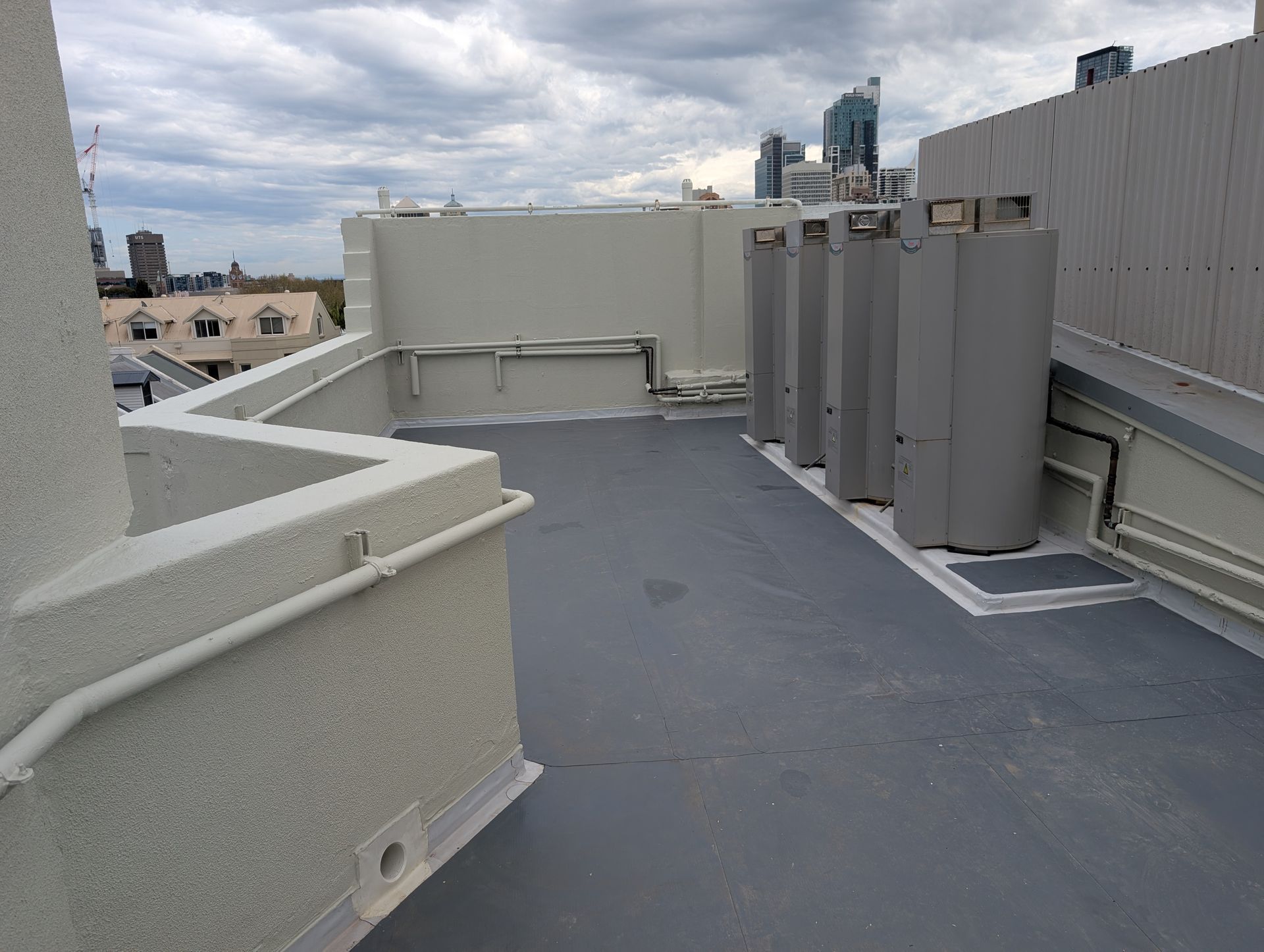 Rooftop terrace with gray floor, white walls, and several cylindrical HVAC units under a cloudy sky