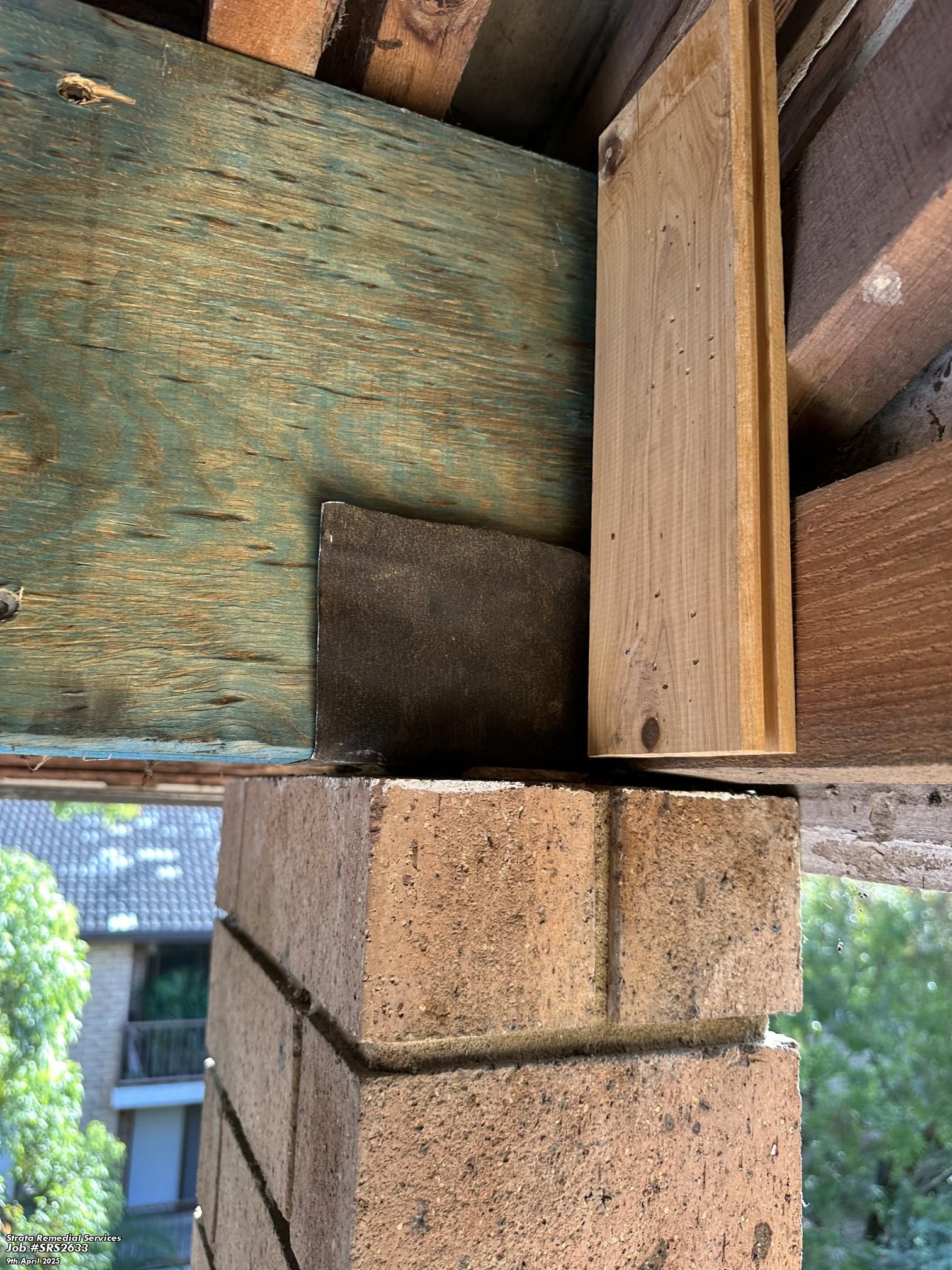 Close-up of a wooden beam joint over a concrete block and weathered wood paneling