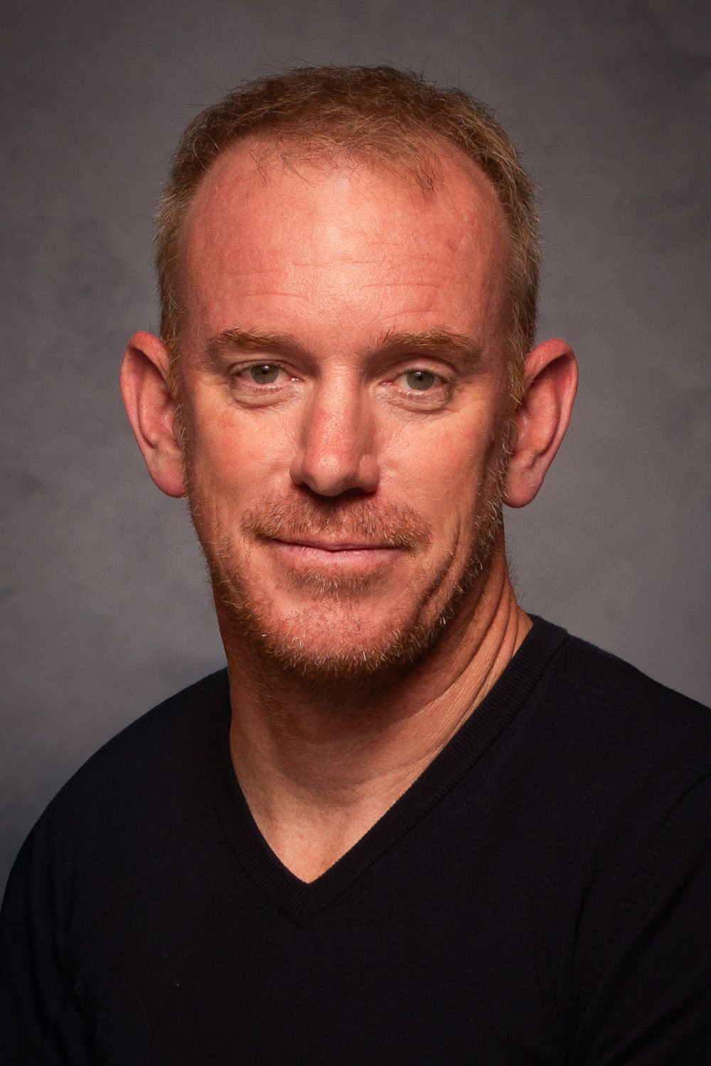 Studio portrait of a man in a black shirt against a gray background