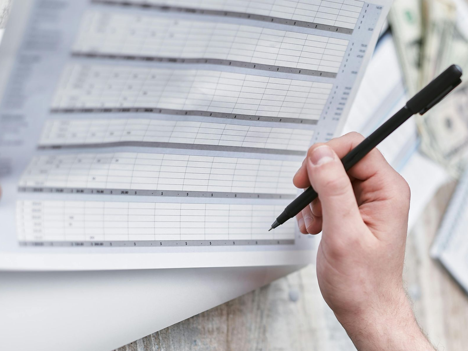 Hand holding a pen over a printed spreadsheet or form on a desk