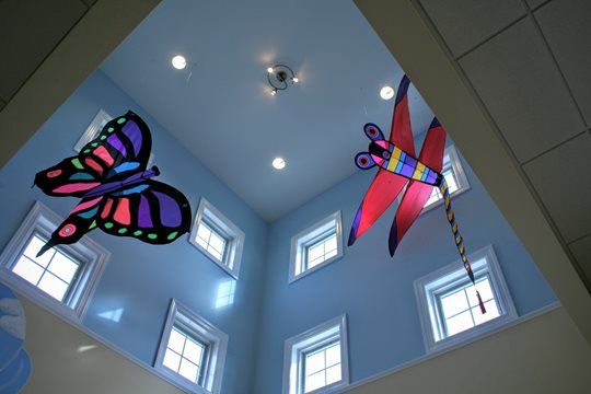 Colorful butterfly and dragonfly kites suspended in a light blue room with several small windows.