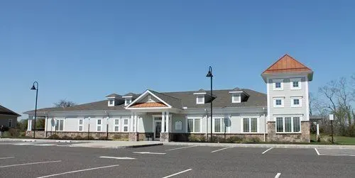 A light blue building with a tower and copper roof on a clear, sunny day. The building has a paved parking lot in front of it.