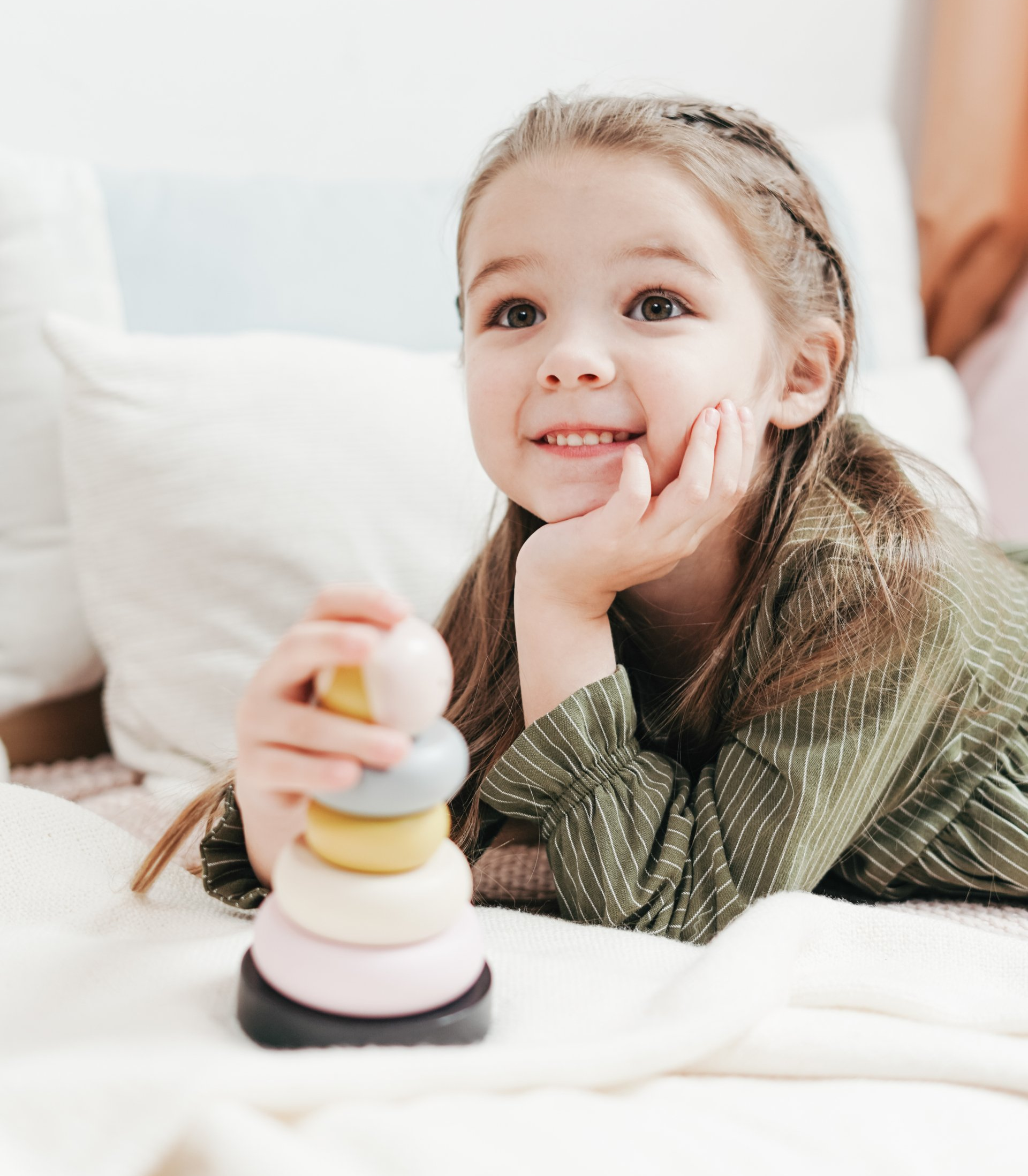 Smiling child resting on a bed beside a colorful stacking toy