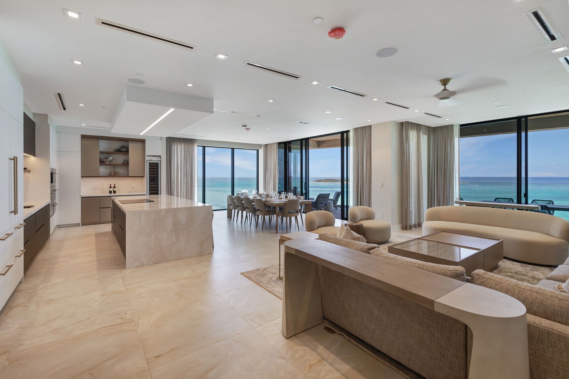 A living room with a couch , table , chairs and a kitchen with a view of the ocean in one of the luxuries properties of Bond Vacations Nassau Bahamas
