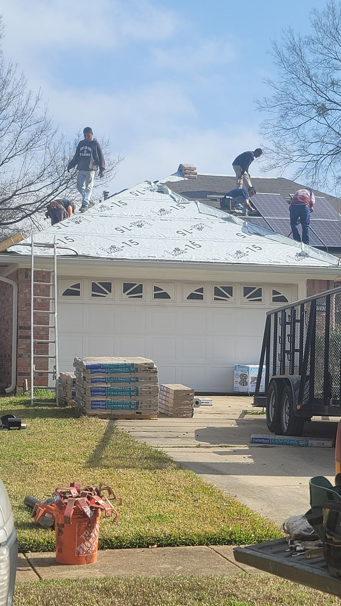 Workers repairing a white garage roof with new shingles and a ladder in the driveway