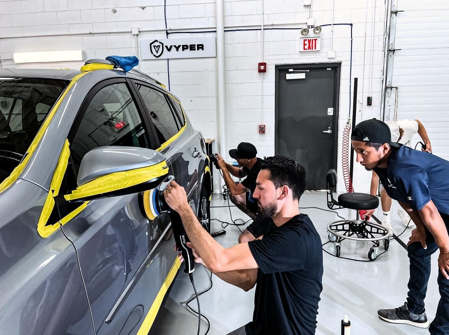 A group of men are polishing a car in a garage.