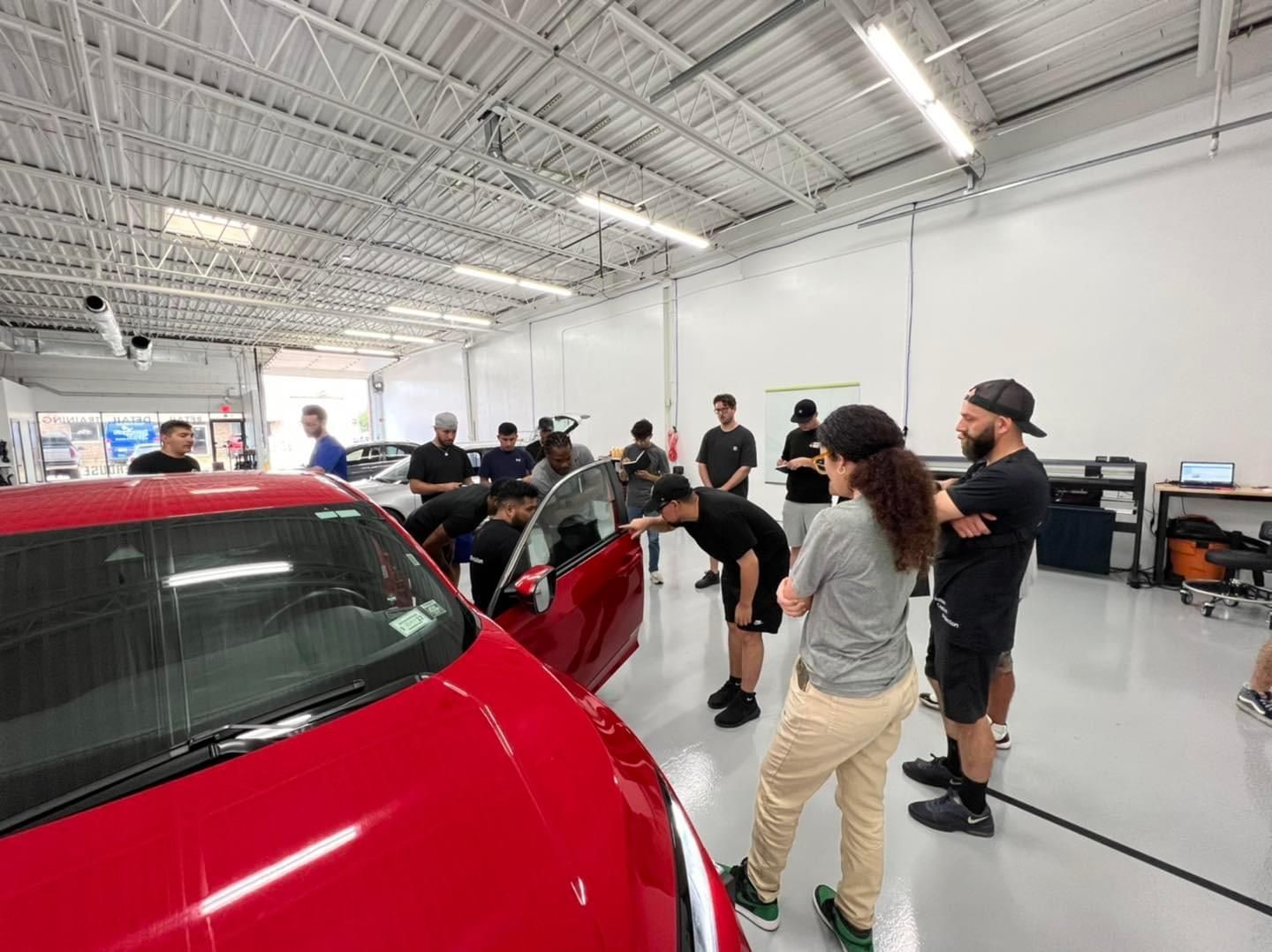 A group of people are standing around a red car in a garage.