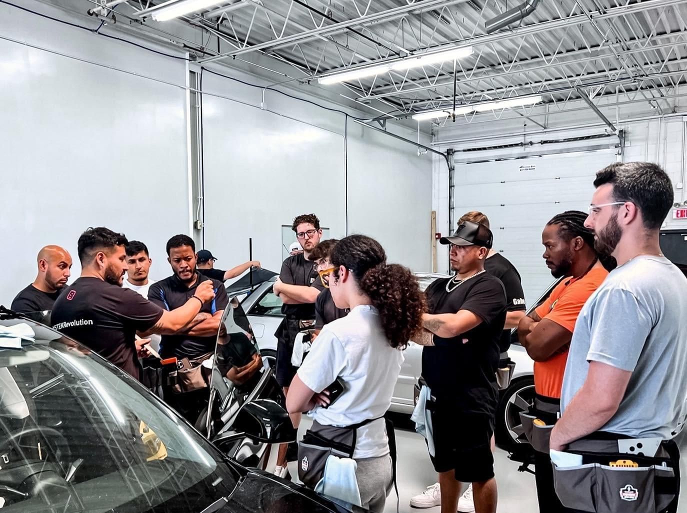 A group of people are standing around a car in a garage.