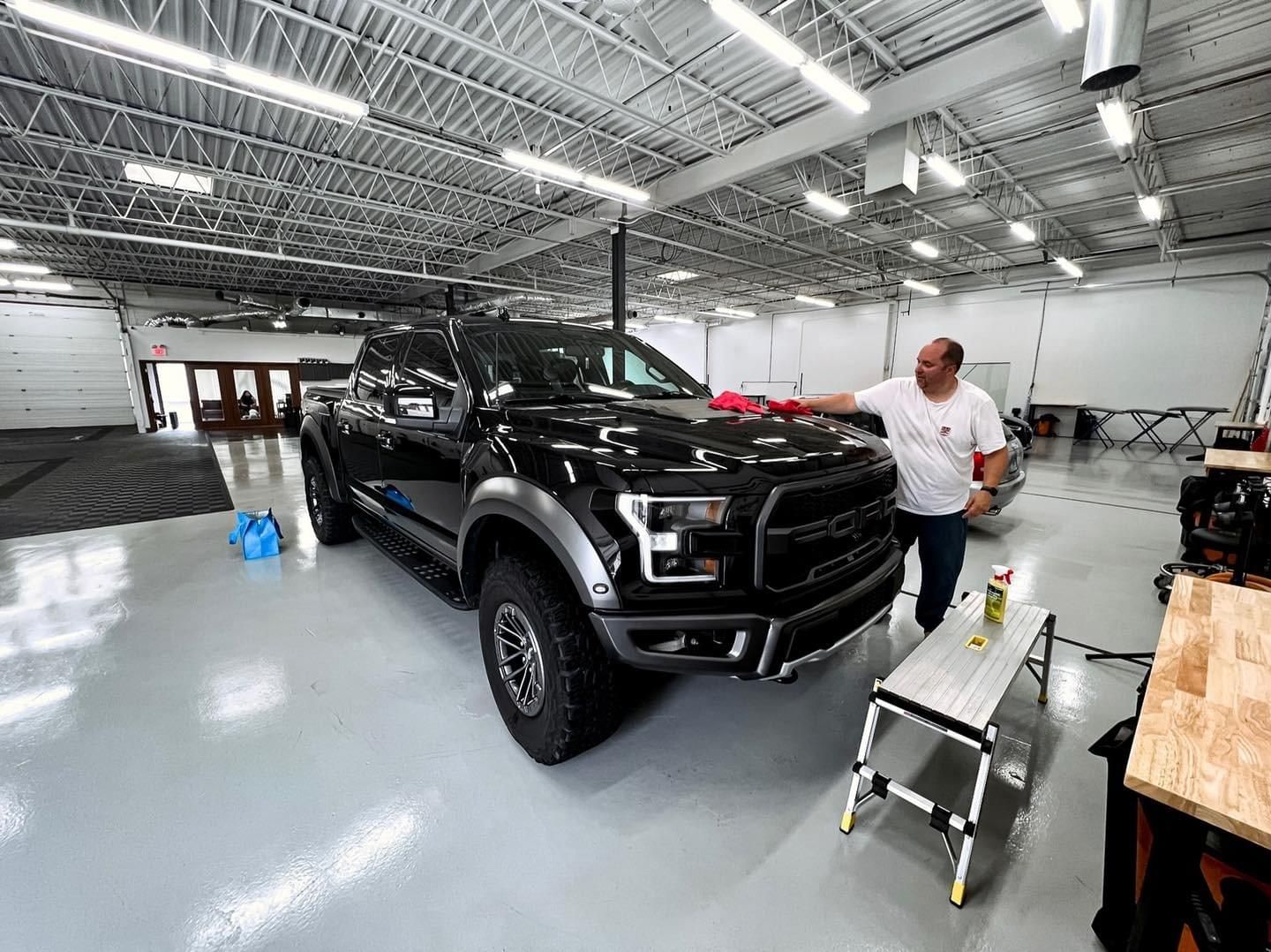 A man is standing next to a black truck in a garage.