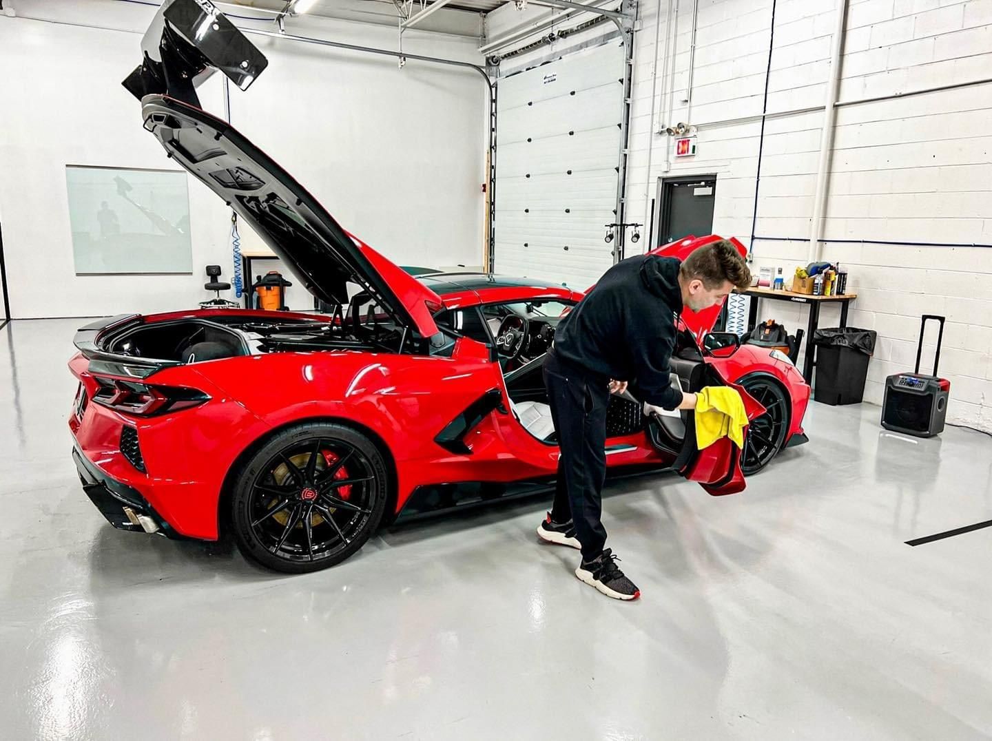A man is cleaning a red sports car in a garage.