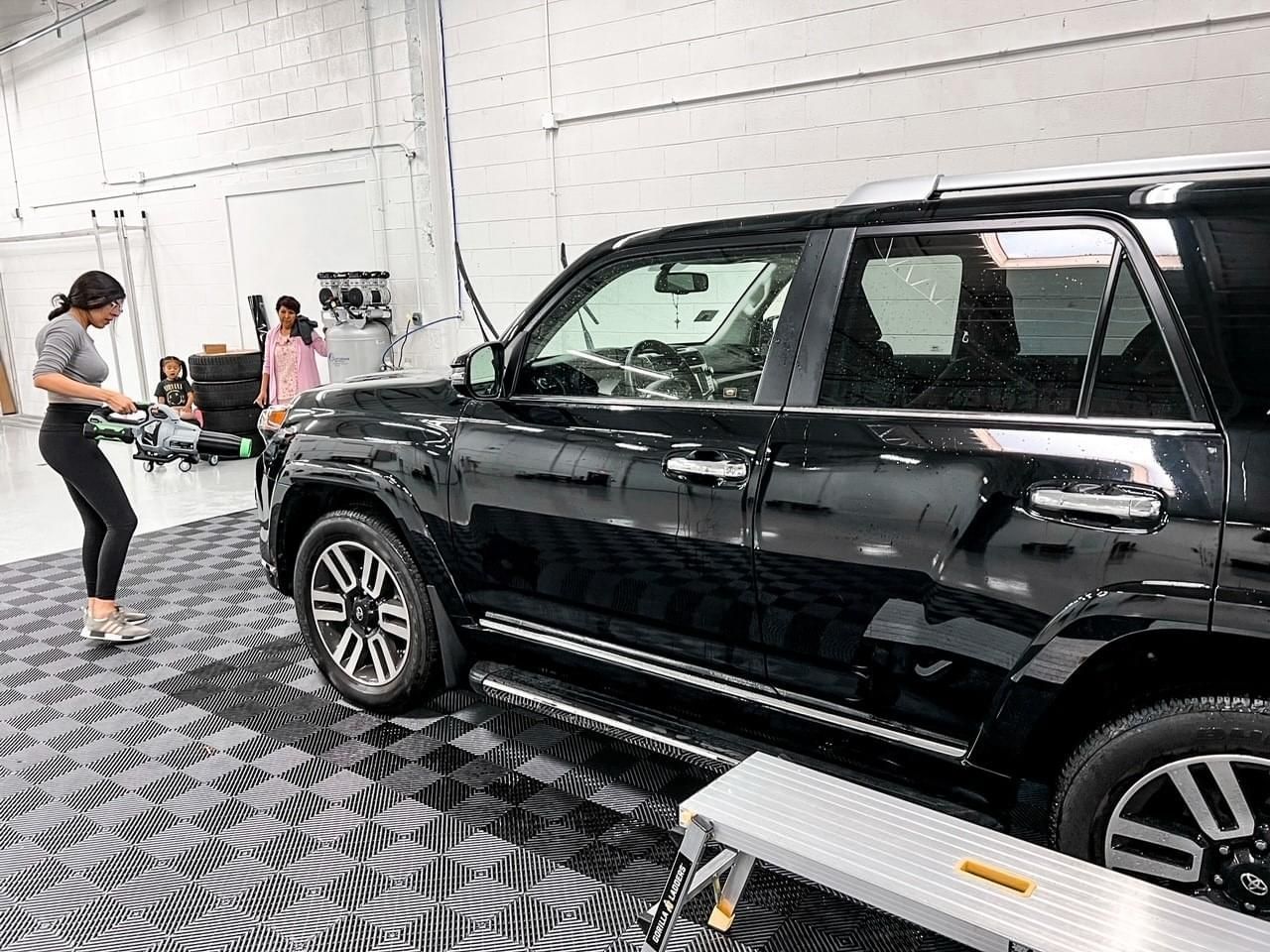 A woman is standing next to a black suv in a garage.