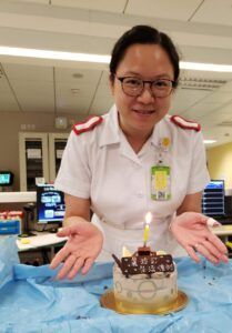 A woman in a white uniform is holding a cake with a candle on it.