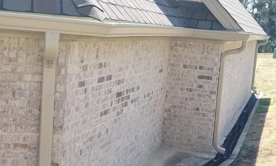 A white brick house with a gutter on the side of it.