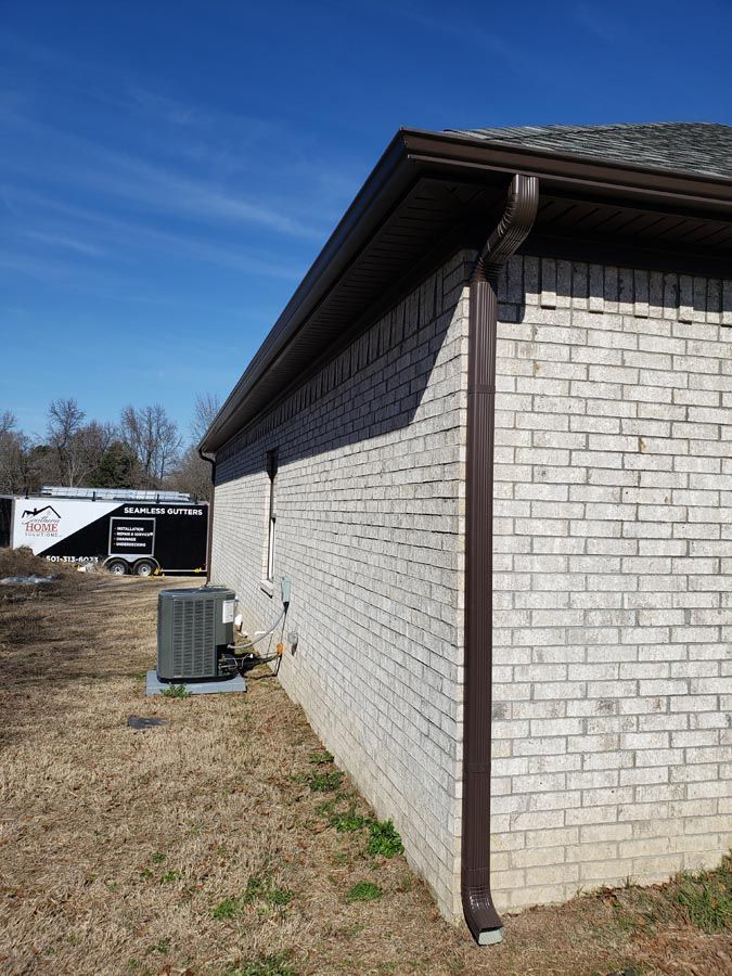A white brick house with a brown gutter on the side
