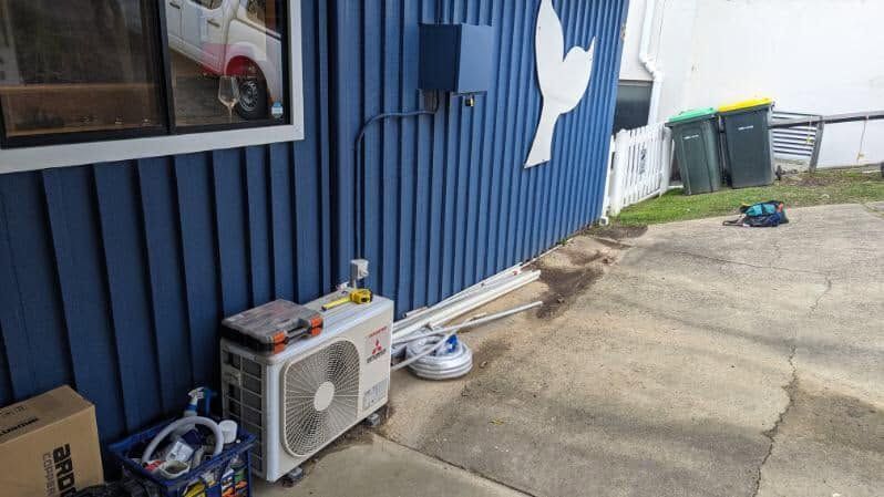 Blue Building Wall With Air Conditioner And Scattered Items — Escarpment Air in Nowra, NSW