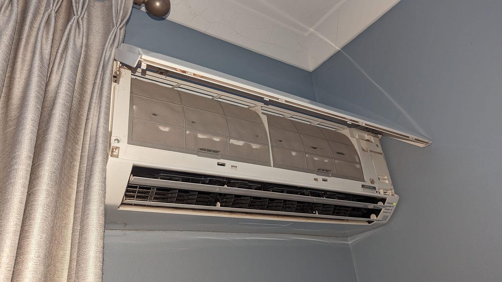 Wall-mounted Air Conditioner Unit On A Light Blue Wall Above A Curtain — Escarpment Air in Campbelltown, NSW