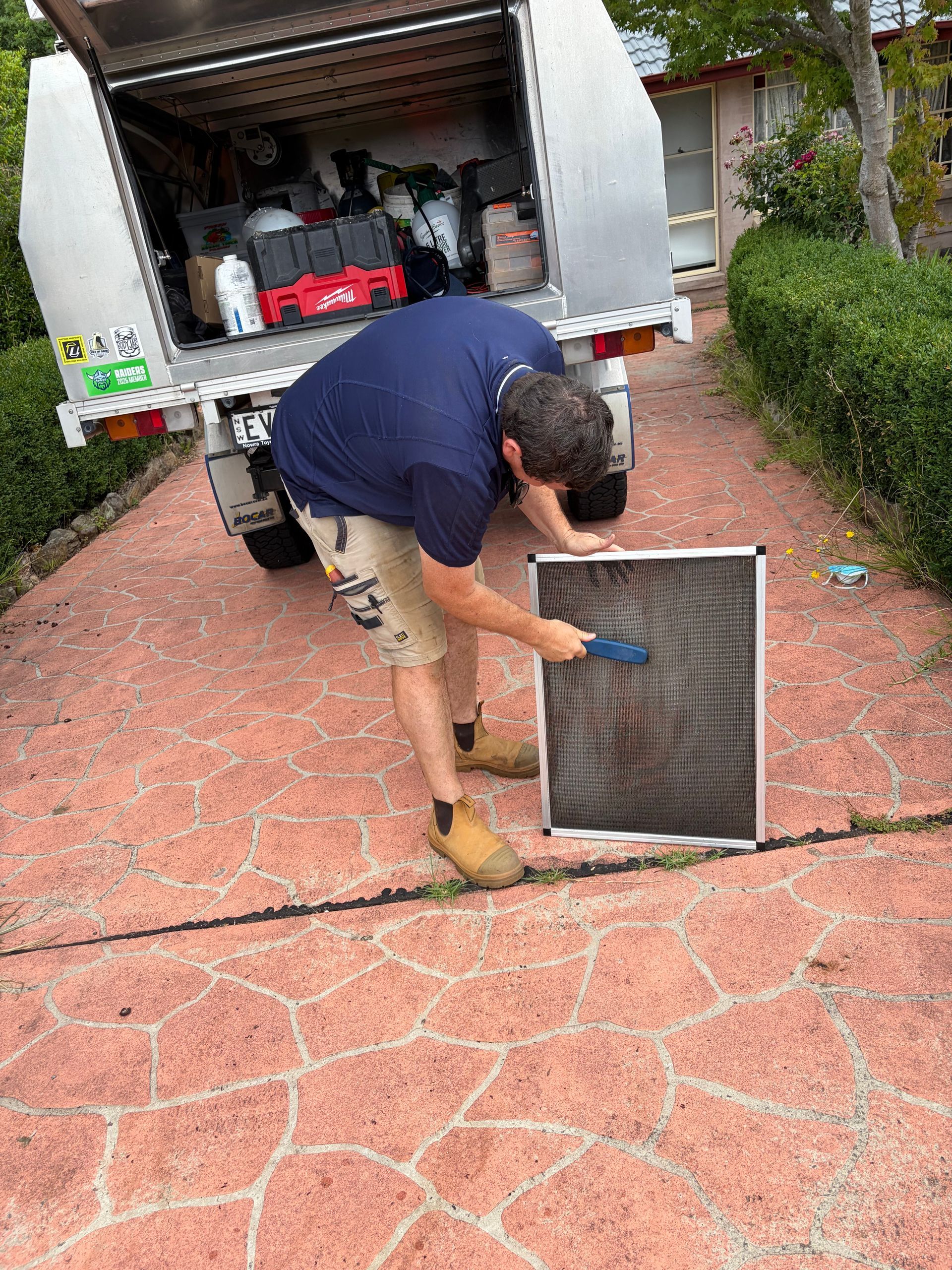 Worker cleaning a truck’s air filter on a driveway, with the van’s rear doors open — Escarpment Air in Shellharbour, NSW
